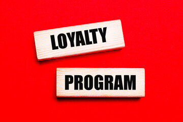 On a bright red background, there are two light wooden blocks with the text LOYALTY PROGRAM