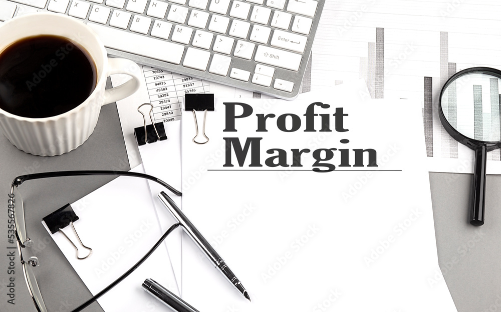 Poster profit margin text on a paper with magnifier, coffee and keyboard on grey background