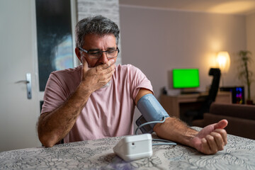 man feeling bad using a home blood pressure machine to check his health in the morning