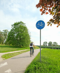 A cyclist rides on a bike path in the summer. A road sign is located on the side of the road. The idea of a healthy lifestyle. High quality photo
