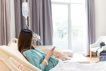 patient woman browsing smartphone while sitting on bed in recovery room of hospital, clinic, giving...