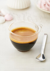 Freshly brewed creamy espresso in a glass coffee cup on white texture background, close up with copy space