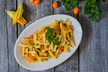 Pasta with courgettes, courgette flowers, yellow datterini tomatoes served in a white plate. Vegetarian recipe