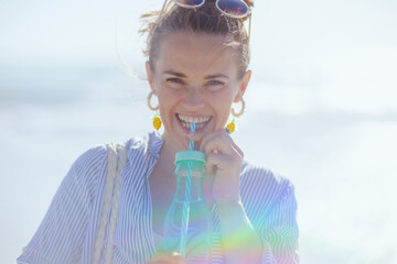 Portrait of smiling modern female with drink at beach