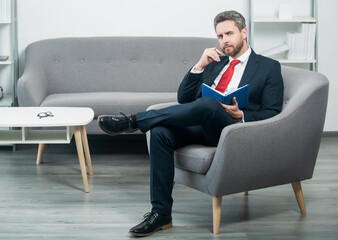 mature boss in suit sit in office making notes in notebook