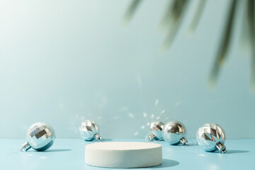 A minimalistic scene of a podium with christmas decorative balls and pine tree on a light blue...