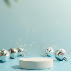 A minimalistic scene of a podium with christmas decorative balls and pine tree on a light blue...