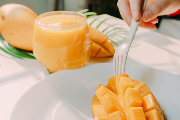 top view and flat lay summer fruit from beauty woman hand hold mango juice and use fork for eat mango slice with shadow of tropical leaf and white background
