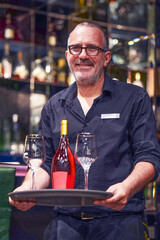 Portrait of man bartender with glasses carries a bottle of red wine with wine glasses. Concept of service
