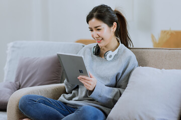 Happy Asian young woman using digital tablet technology sitting on the couch at home. 