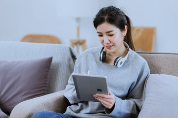Happy Asian young woman using digital tablet technology sitting on the couch at home. 