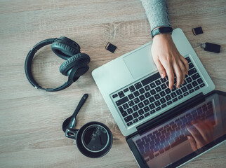 Girl using laptop with coffee cup, headphones and sd cards on the desk