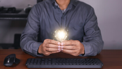 The hand of a man with a light bulb and he is using a notebook computer. Thinking differently...
