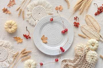 Ivory plate with dry leaves and berries, Autumn background. Off white textile tablecloth with natural Fall decor. Flat lay with pumpkins in net bag, dry leaves, macrame pads, straw and wheat ears.