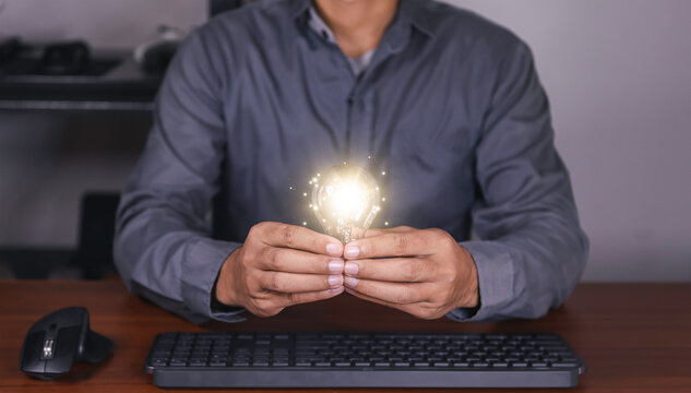 The hand of a man with a light bulb and he is using a notebook computer. Thinking differently creates inspiration and ideas. technologies can always come from creative and different ideas.