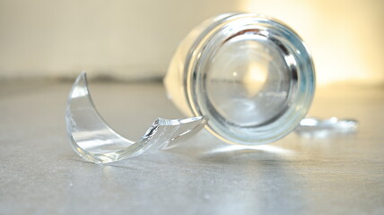 Closeup of empty cracked drinking glass isolated on grey tile background with sunlight, beverage...