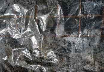 Silberne Plastikfolie vor braunen Fenstergitterstäben