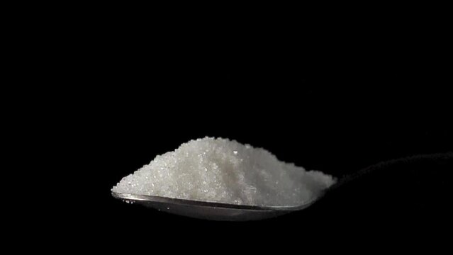 Sugar in a spoon on isolated black background