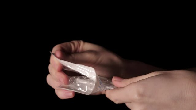 Nurse opens syringe on black background close up