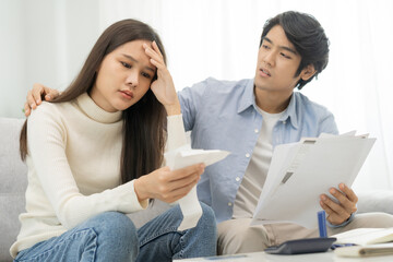 Stressed financial owe asian young couple love hand in holding bills, sitting on sofa together, stressed and confused by calculate expense, mortgage or loan. Debt, bankrupt or bankruptcy people.