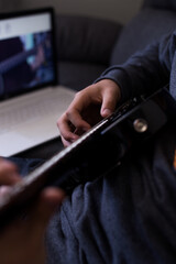 Young man learning to play guitar online with his laptop and guitar. Concept of virtual education and music.