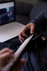 Young man learning to play guitar online with his laptop and guitar. Concept of virtual education and music.