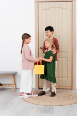 Interracial kids giving shopping bag and present to friend at home