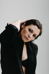 brunette woman with a wet hairstyle in the studio enjoys the rays of the sun in a business jacket.
