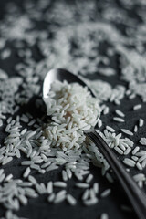 White rice scattered on the table and a small spoon, black background