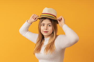 young beautiful elegant girl straightens her hat on her head with both hands, stands against a yellow background. travel concept