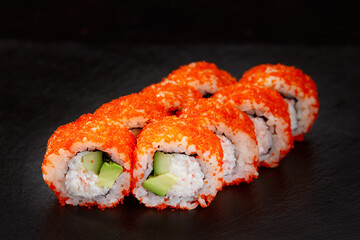 appetizing sushi roll california with avocado shrimp cheese and masago caviar on a black background.