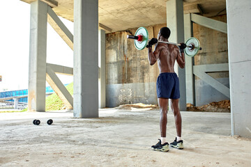 Athletic black young man lifting a heavy-weight barbell in outdoor gym under the bridge. Healthy...