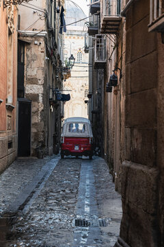 Old Ape driving down a narrow street in the center of the old town of Tropea. Vintage car for transportation and tourist attraction. Travel vacation in Calabria, Southern Italy.