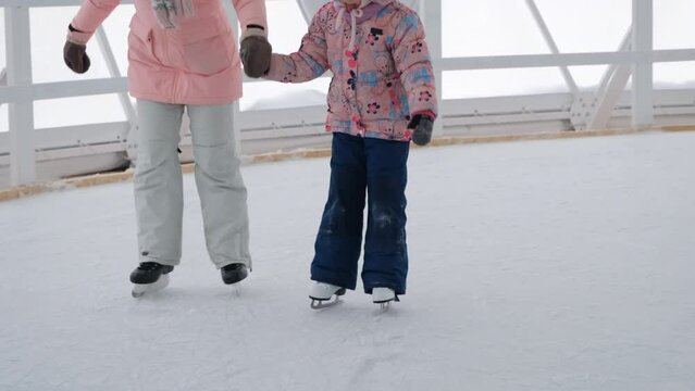 Young caucasian woman with little daughter holding hands and enjoying ice skating at indoor ice rink. Winter family activities concept