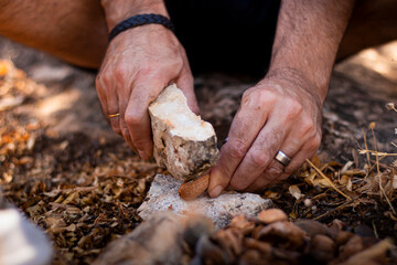 Man's hands in the field hitting an almond with a stone to open it and eat its fruit.