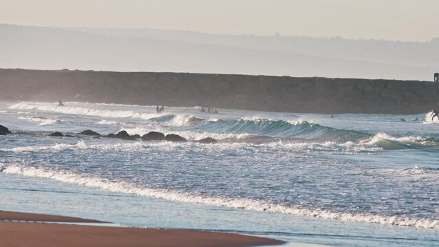 Swimmers and Surfers on ocean wave at sunset, Atlantic Ocean - coast of Costa da Caparica, Portugal