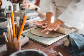 View of female hands works with clay makes future ceramic plate, ceramic artist makes classes of hand building in modern pottery workshop, creative people handcrafted design