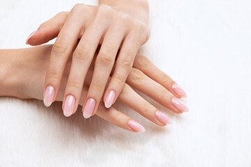 Girl's hands with a beautiful pale pink manicure. In the hands of white fur. the nail extension procedure in a beauty salon. Professional hand care. - obrazy, fototapety, plakaty