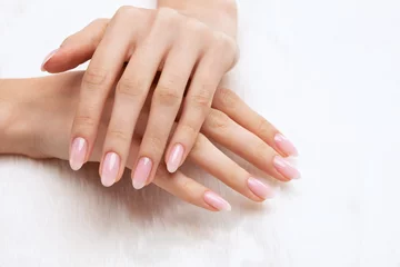 Poster Girl's hands with a beautiful pale pink manicure. In the hands of white fur. the nail extension procedure in a beauty salon. Professional hand care. © Dimid