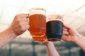 Male hands holding three glass mugs of light and dark draft beer. Beer toast, cheers.