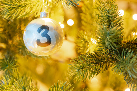 eine wei&szlig;e Weihnachtskugel am Christbaum, mit einer Zahl (3) f&uuml;r den Adventskalender