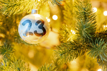 eine weiße Weihnachtskugel am Christbaum, mit einer Zahl (23) für den Adventskalender