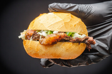 hand holding delicious beef sandwich with tomato and onion on table, vinaigrette made on fire