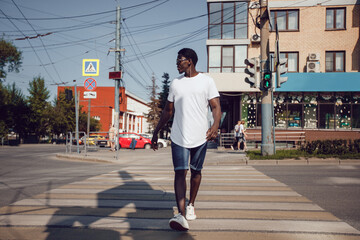 Fototapeta premium African american man in a white t-shirt walking down the street. Mock-up.