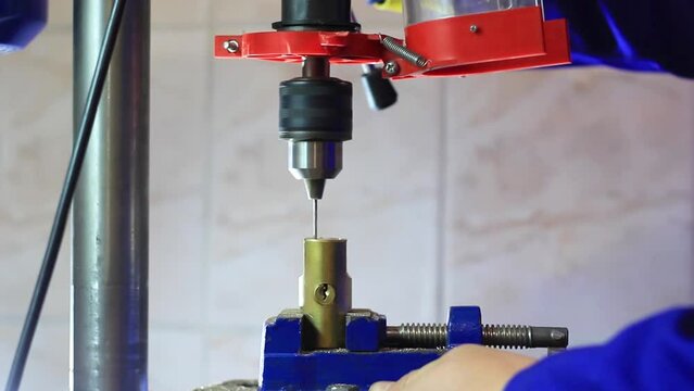 The drill drills a hole in a metal lock that is clamped with a vise
