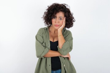 Very bored young beautiful woman with curly short hair wearing green overshirt over white wall...