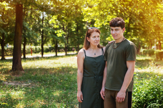 Concept Of Strong Family Relationship Between Mother And Son. A Woman And Her Teenage Son Are Walking In The Park And Talking