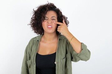 young beautiful woman with curly short hair wearing green overshirt over white wall pointing...