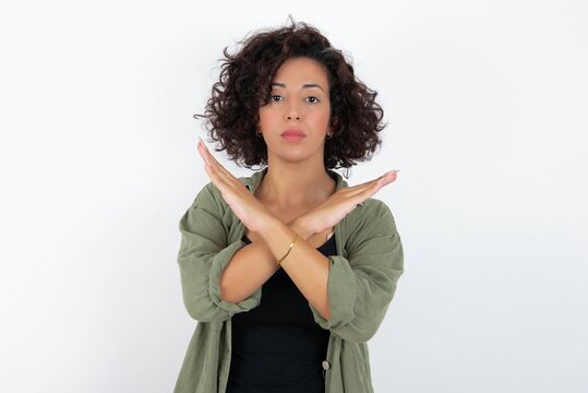 young beautiful woman with curly short hair wearing green overshirt over white wall Rejection expression crossing arms doing negative sign, angry face