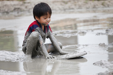 cute happy asian little boy enjoying to play in the mud at playground. child learning in nature at...